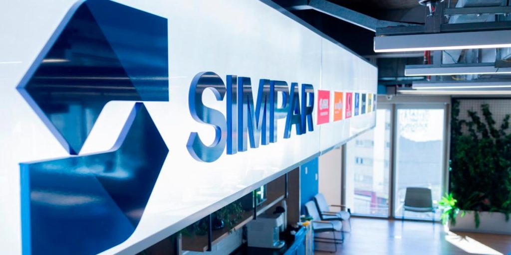 Refeitório do escritório da SIMPAR, com foco no banner com o logo da empresa e de suas controladas. 
